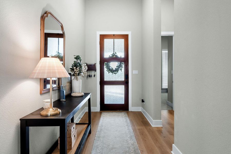 Entryway featuring wood-finish flooring, a dark wood-paneled door with frosted glass inserts, and light-toned wall finishes