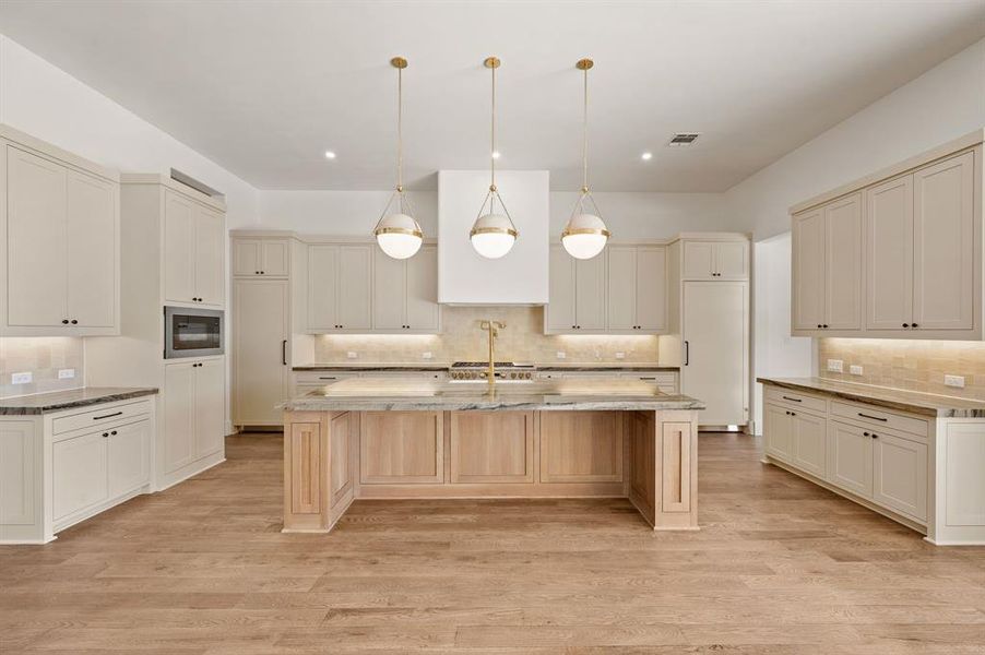 Kitchen with hanging light fixtures, light stone counters, an island with sink, a kitchen bar, and light wood-type flooring