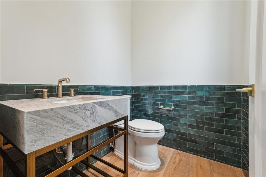 This elegant powder room off the game room features stunning emerald green wainscoting wall tile that adds a pop of color and sophistication. A marble countertop with brass fixtures complements the design, while a nearby window allows natural light to brighten the space.