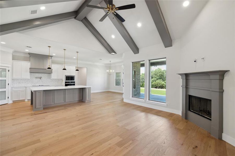 Unfurnished living room with ceiling fan with notable chandelier, high vaulted ceiling, light wood-type flooring, ornamental molding, and beam ceiling