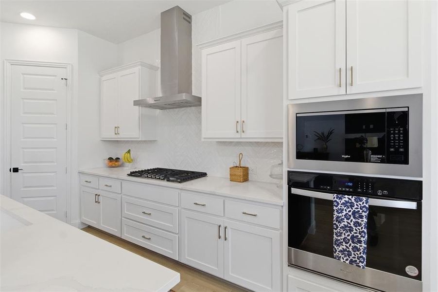 Modern kitchen featuring white cabinetry, light-toned countertops, a built-in oven, a built-in microwave, and a gas cooktop with a stainless steel range hood