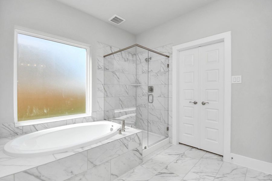 Expansive walk-in shower surrounded with tile and the distinct garden tub adorned with unique details. Sample photo of completed home with similar floor plan. Actual colors and selections may vary.