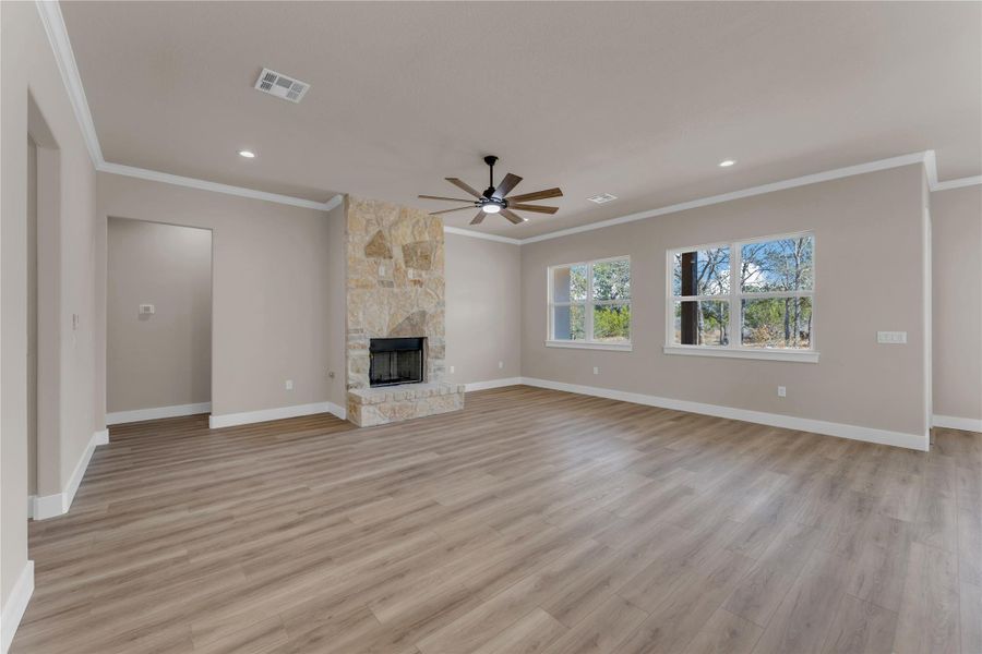 Unfurnished living room featuring light wood finished floors, crown molding, a ceiling fan, a fireplace, and recessed lighting