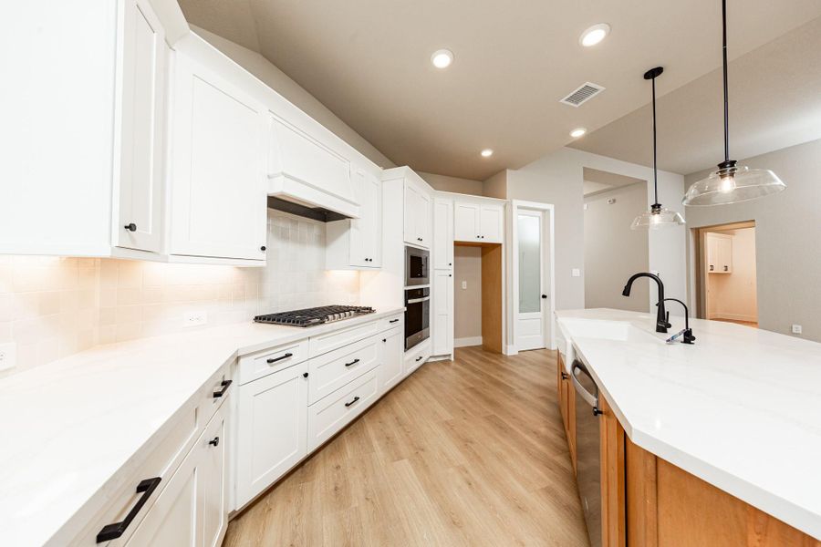 A spacious central island offers prep space and houses a sleek farmer's sink and a dishwasher. Recessed and contemporary pendant lights ensure a well-lit environment.