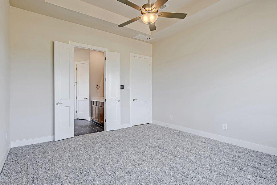 Soft carpet underfoot and neutral tones create a restful retreat, complete with double doors leading to the en suite bath.