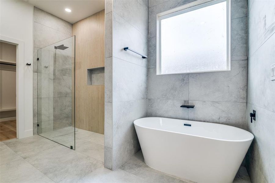 Full bathroom with walk in shower, a freestanding tub, a walk in closet, and tile walls