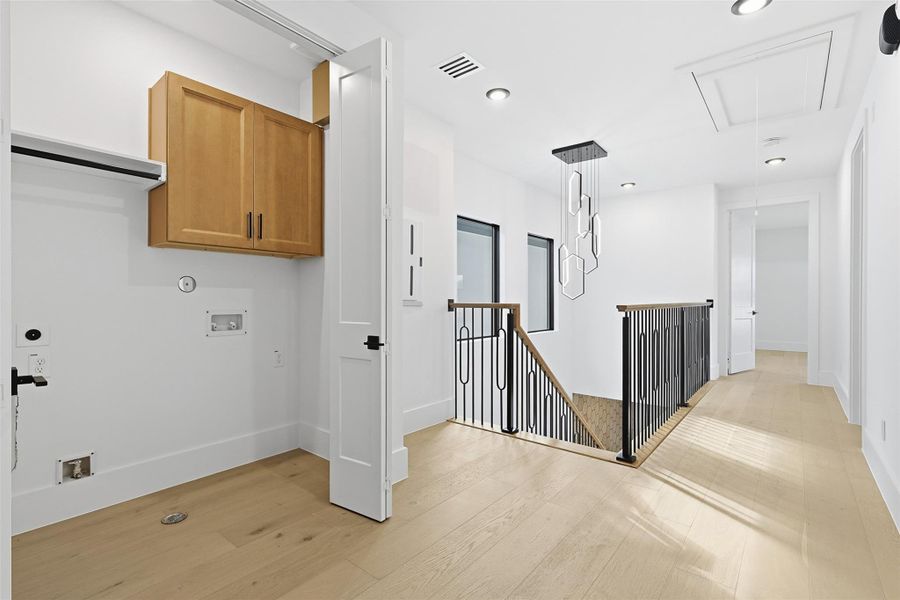 The second-floor landing includes a laundry area with wood cabinetry and a modern geometric chandelier over the stairs.