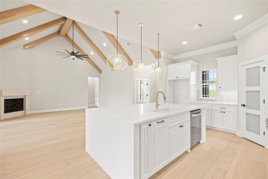 Kitchen featuring a kitchen island with sink, open floor plan, white cabinets, decorative light fixtures, and beamed ceiling Kitchen featuring a kitchen island with sink, open floor plan, white cabinets, decorative light fixtures, and beamed ceiling