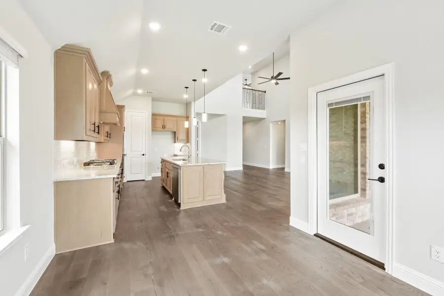 Open-concept kitchen with light wood cabinets, center island, hardwood floors, and vaulted ceiling with pendant lights Open-concept kitchen with light wood cabinets, center island, hardwood floors, and vaulted ceiling with pendant lights