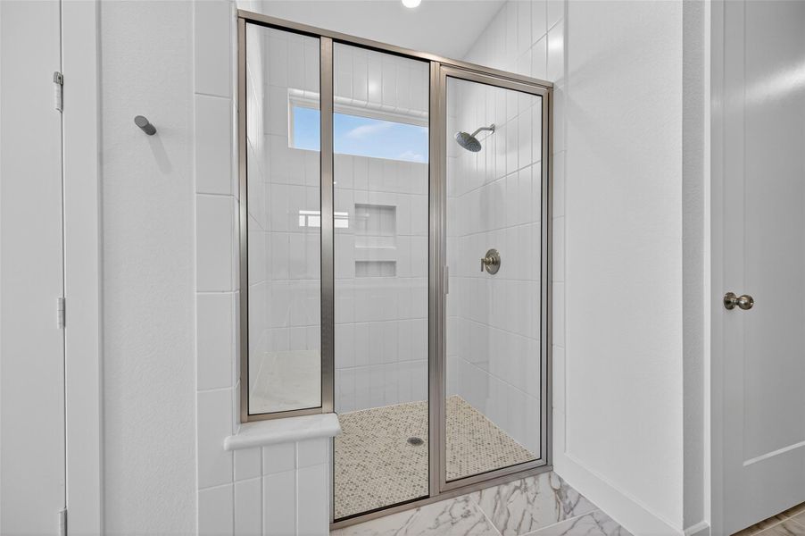 The primary bathroom features a sleek walk-in shower with elegant tile and a glass enclosure. Its modern design and bright finish create a fresh, spa-like feel.