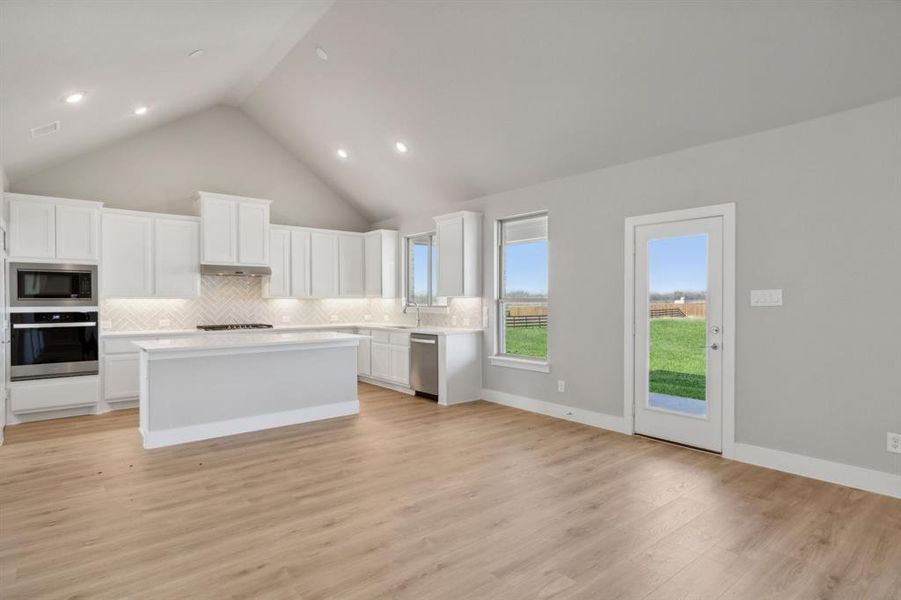 Kitchen with high vaulted ceiling, white cabinets, light hardwood / wood-style flooring, a kitchen island, and stainless steel appliances