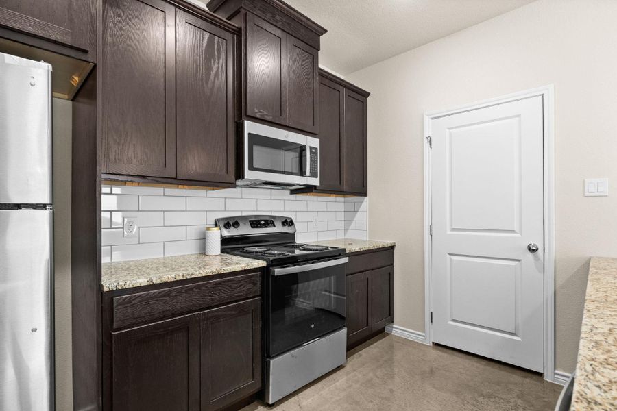 Kitchen featuring stainless steel appliances, backsplash, light stone counters, and dark brown cabinets