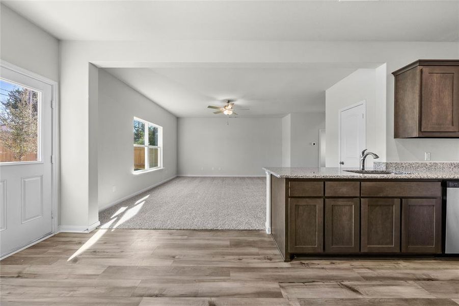 Kitchen featuring stainless steel dishwasher, a ceiling fan, a sink, dark brown cabinets, and light stone countertops