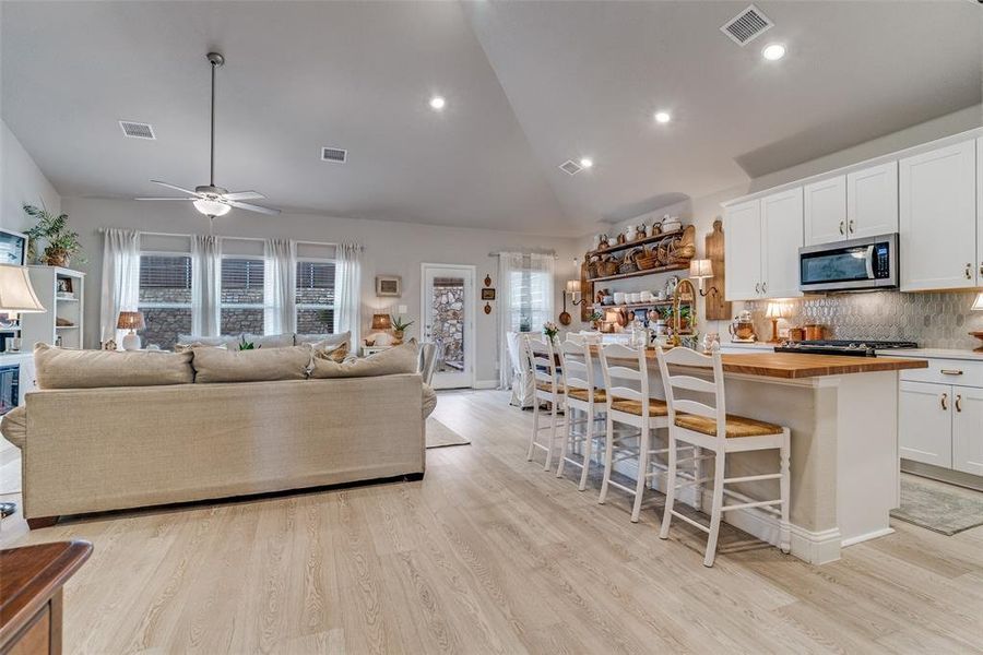 Kitchen featuring butcher block counters, a kitchen breakfast bar, an island with sink, white cabinets, and open floor plan Kitchen featuring butcher block counters, a kitchen breakfast bar, an island with sink, white cabinets, and open floor plan