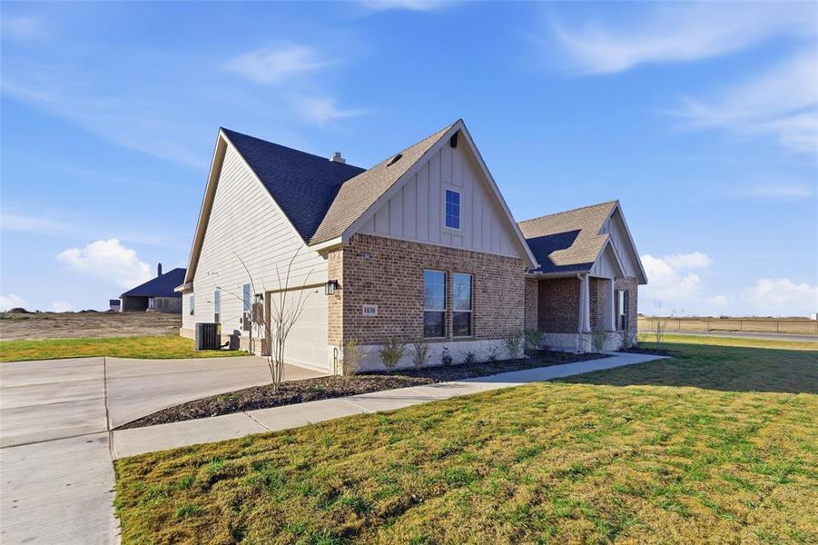 View of front facade with board and batten siding, brick siding, concrete driveway, a front lawn, and a shingled roof