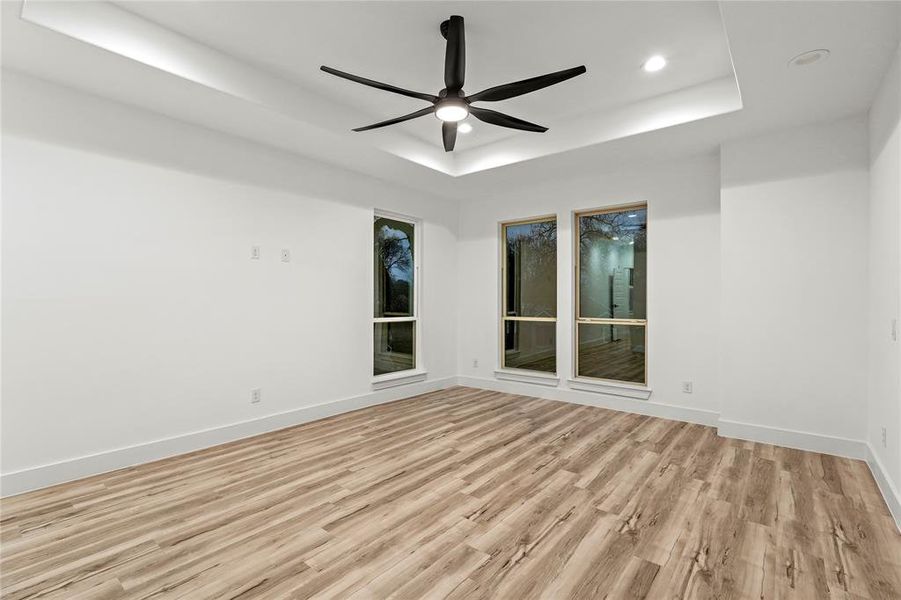 Spare room with a raised ceiling, ceiling fan, and light wood-type flooring