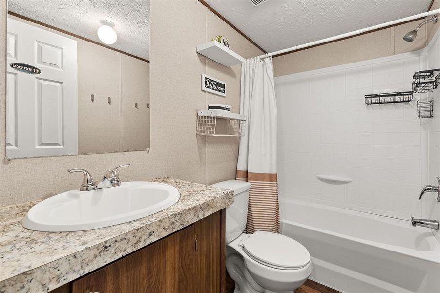 Full bathroom featuring a textured ceiling, shower / bath combo with shower curtain, and vanity