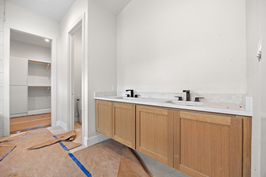 Dual vanity with wood-finish cabinetry, light-toned countertop, and matte black fixtures