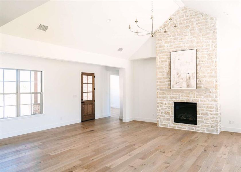 Unfurnished living room featuring a stone fireplace, light hardwood / wood-style flooring, high vaulted ceiling, and an inviting chandelier