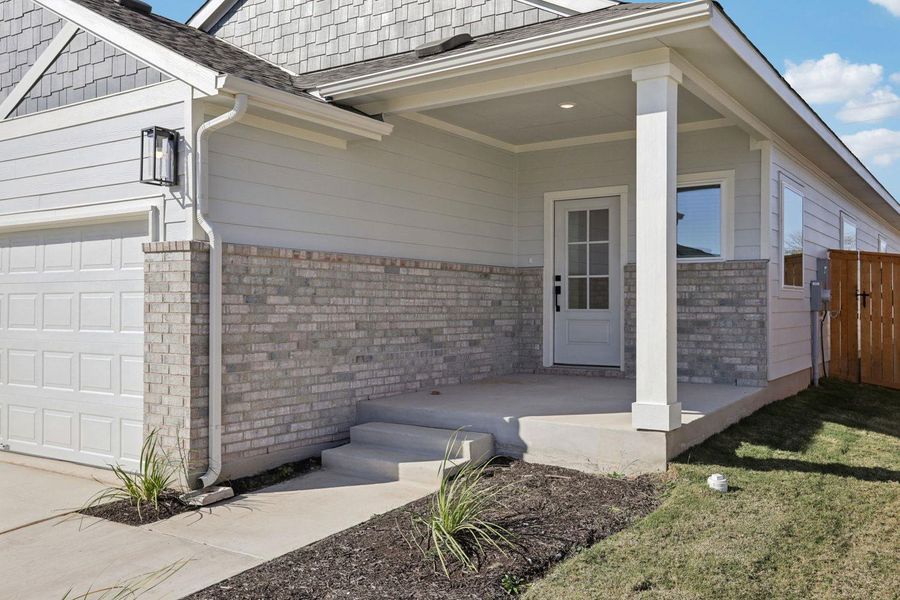 View of exterior entry with brick siding, an attached garage, a shingled roof, and a gate