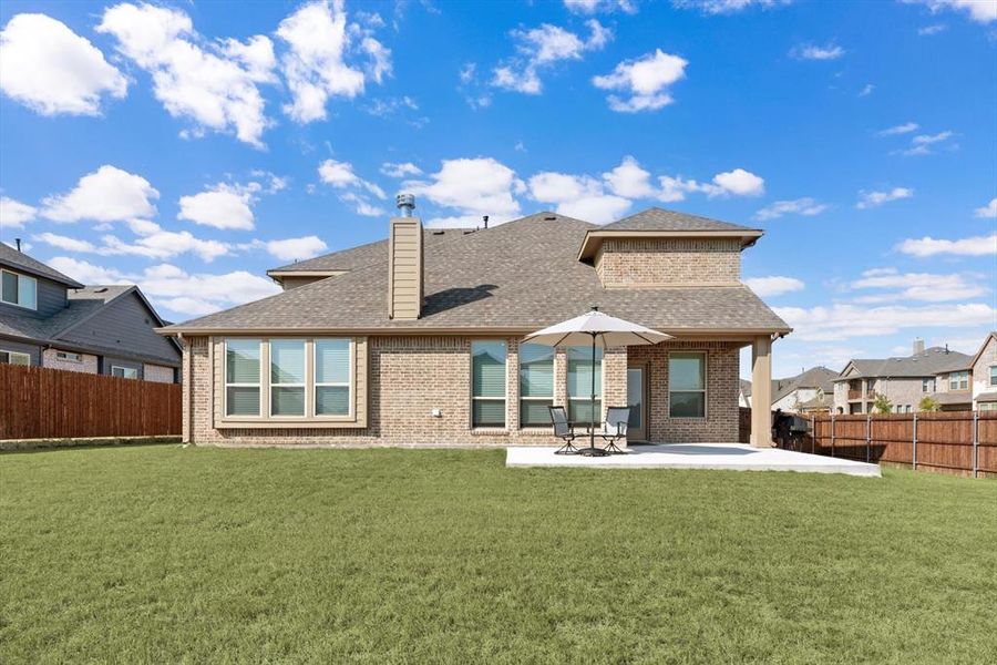 Rear view of all brick home featuring a covered and extended open patio and a big backyard! Fencing is stained with steel posts.