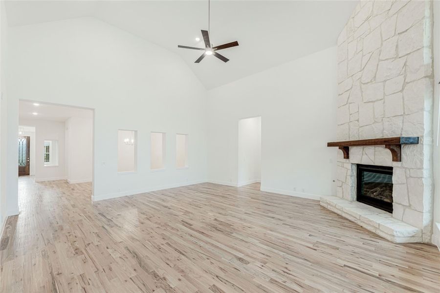 Open living room with vaulted ceiling, stone fireplace, ceiling fan, and light hardwood floors