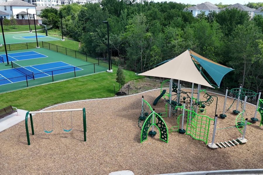 Aerial photo of community playground including swing set, and sports court with trees