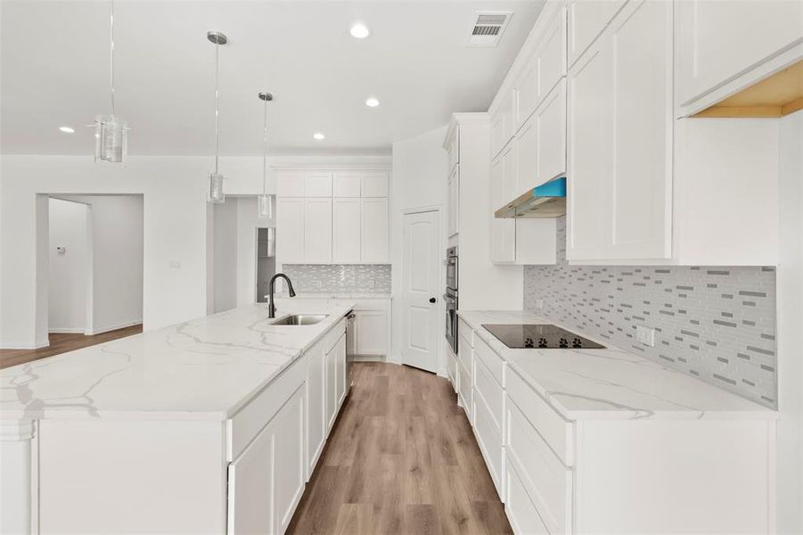 Kitchen with a large island with sink, decorative light fixtures, white cabinetry, and sink