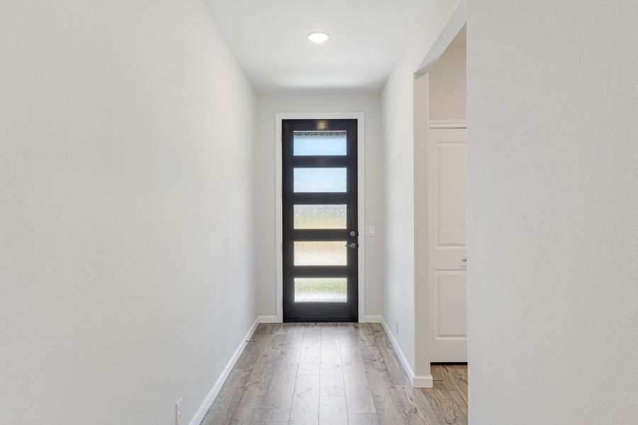 Narrow entryway with black front door featuring four glass panels and light wood floors