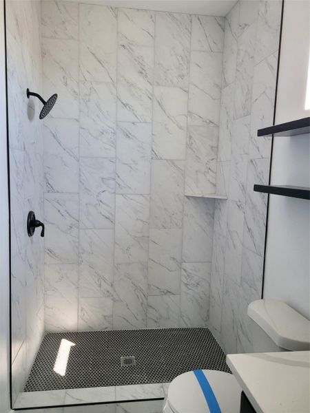 A striking shower with marble-look wall tiles and a contrasting mosaic floor creates a clean, modern aesthetic. A striking shower with marble-look wall tiles and a contrasting mosaic floor creates a clean, modern aesthetic.