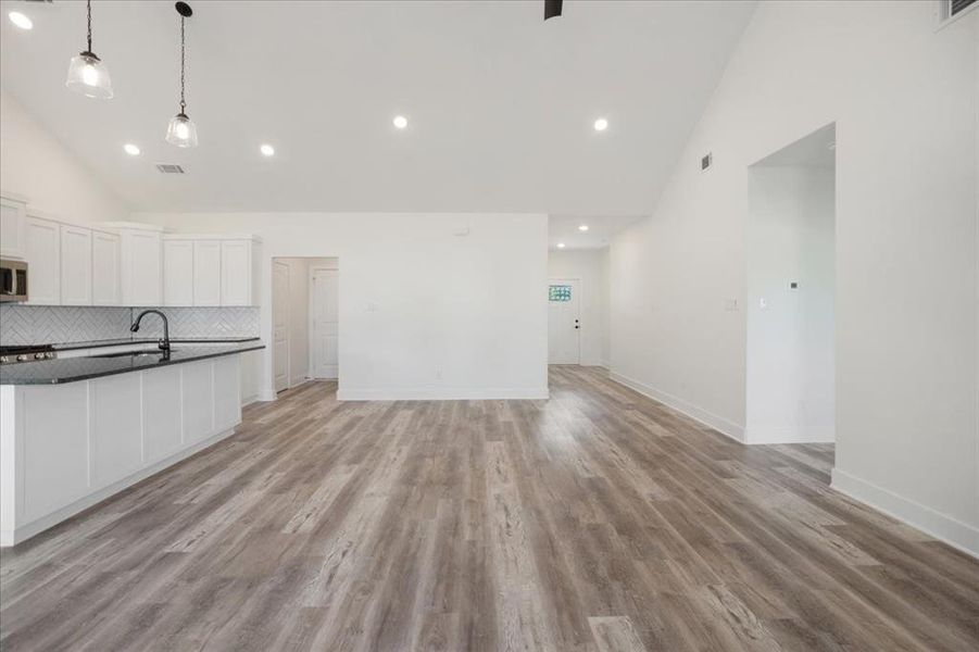 Kitchen featuring high vaulted ceiling, white cabinets, decorative backsplash, light wood-style flooring, and hanging light fixtures