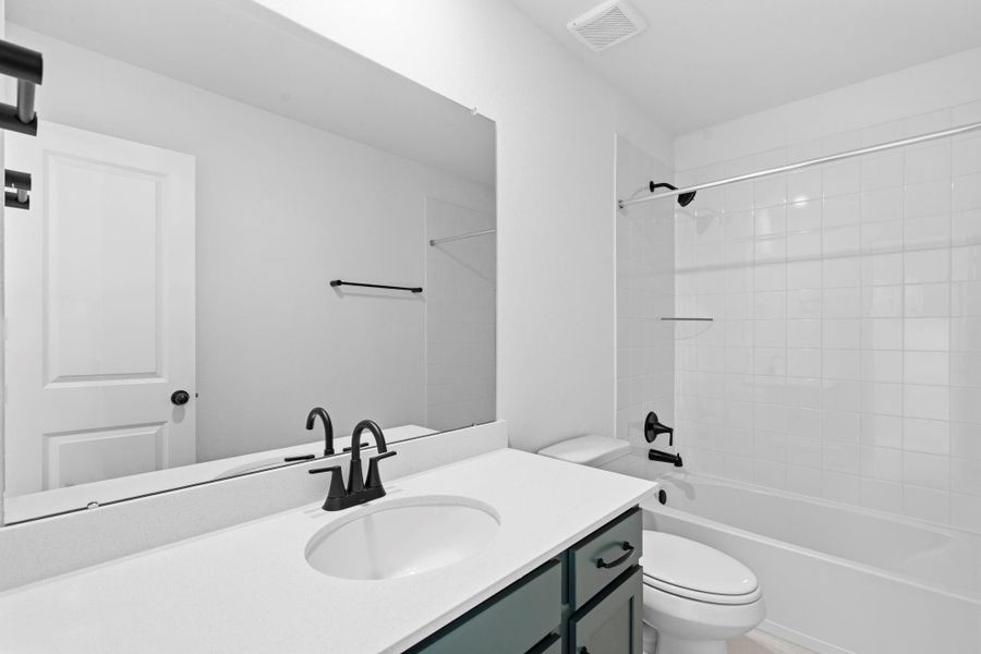 Bright and contemporary second bath with green cabinets, light countertops, and a convenient shower/tub combo.