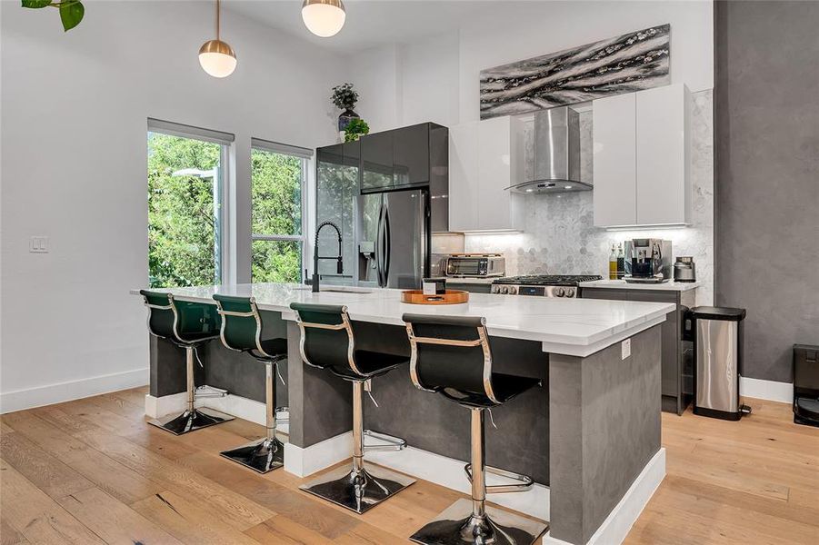 Kitchen featuring an island with sink, a breakfast bar area, modern cabinets, pendant lighting, and wall chimney exhaust hood Kitchen featuring an island with sink, a breakfast bar area, modern cabinets, pendant lighting, and wall chimney exhaust hood