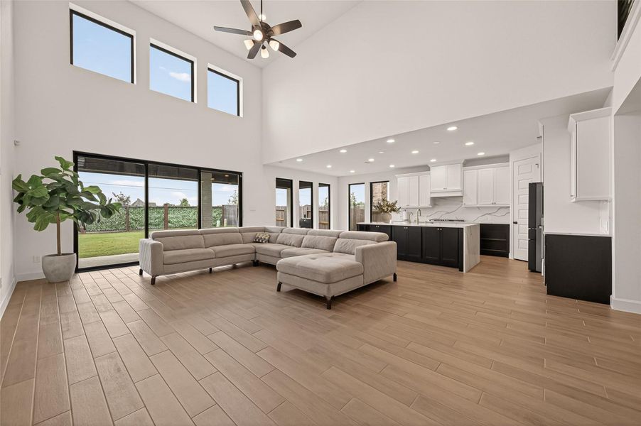 This spacious, open-concept living area features high ceilings, large windows for ample natural light, and elegant wood-look flooring. The modern kitchen boasts sleek cabinetry, a large island, and recessed lighting, seamlessly connecting to the living space.