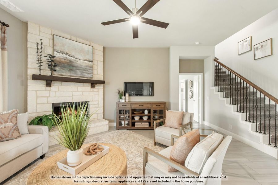 Living room with stone fireplace, ceiling fan, staircase, and neutral furnishings on tile floors