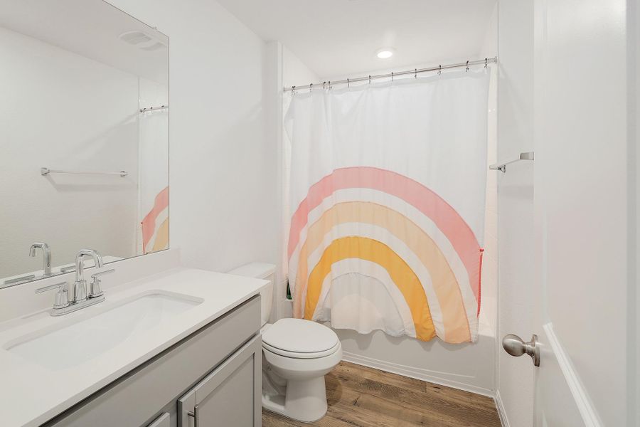 Bathroom featuring a white bathtub with shower, a vanity with a light gray cabinet and white countertop, wood-finish flooring, and a flush-mounted ceiling light Bathroom featuring a white bathtub with shower, a vanity with a light gray cabinet and white countertop, wood-finish flooring, and a flush-mounted ceiling light