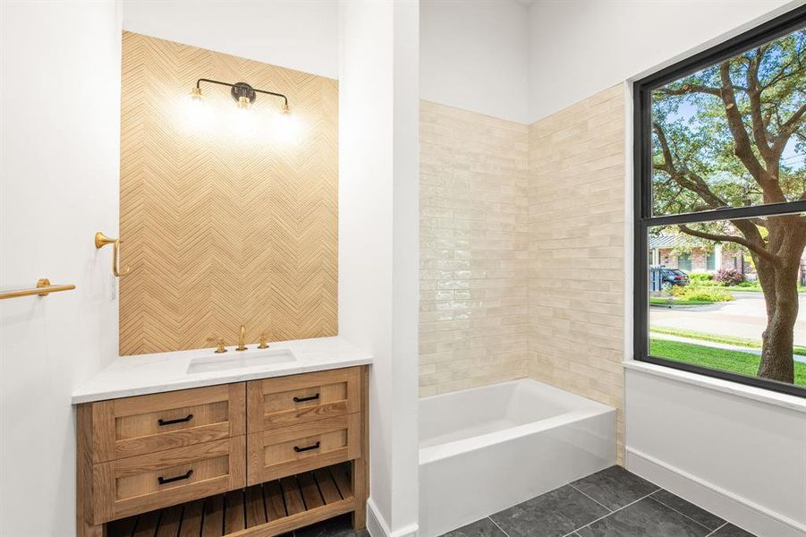 guest bedroom ensuite bath downstairs with dark tile patterned flooring, vanity, and washtub / shower combination guest bedroom ensuite bath downstairs with dark tile patterned flooring, vanity, and washtub / shower combination
