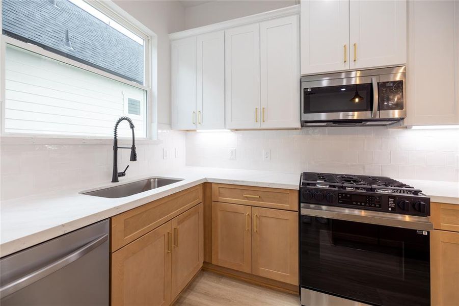 This kitchen showcases natural wood cabinetry on the bottom, paired with sleek Calacatta quartz countertops and white cabinetry on top, all accented with gold hardware. A farmhouse sink beneath a window adds charm, while the gas range ensures a high-quality cooking experience.