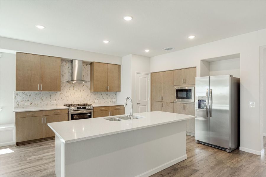 Kitchen with large center island, stainless steel appliances, tan cabinets, and decorative tile backsplash