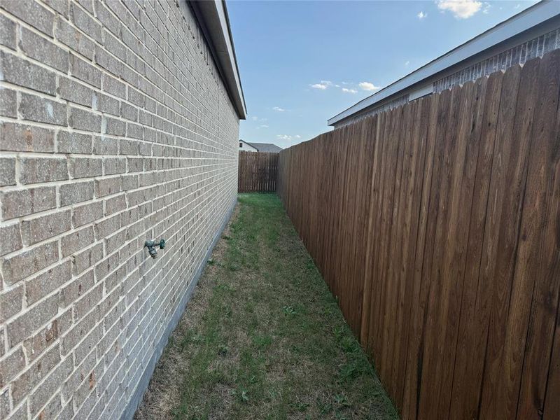 Side yard featuring a brick exterior, wood privacy fencing, and a grassy strip Side yard featuring a brick exterior, wood privacy fencing, and a grassy strip