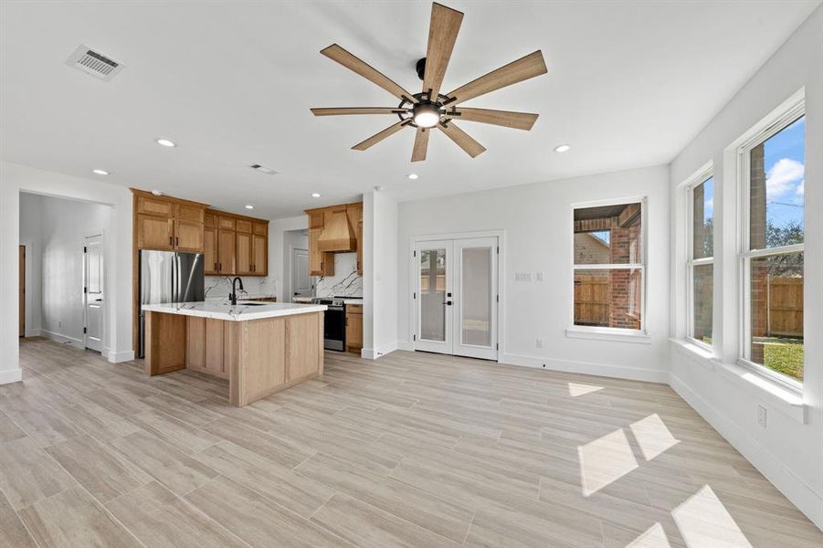 Kitchen with brown cabinets, visible vents, appliances with stainless steel finishes, a sink, and an island with sink