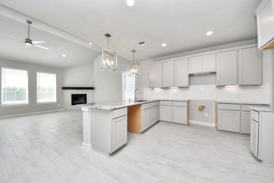 This kitchen is truly a chef's dream! This haven Boasts high ceilings, recessed & pendant lighting, stained wood cabinets, granite countertops, stainless steel appliances, a modern tile backsplash.  All of this overlooks your expansive family room, creating a perfect space for culinary delights and family gatherings. Sample photo of completed home with similar floor plan. Actual colors and selections may vary.
