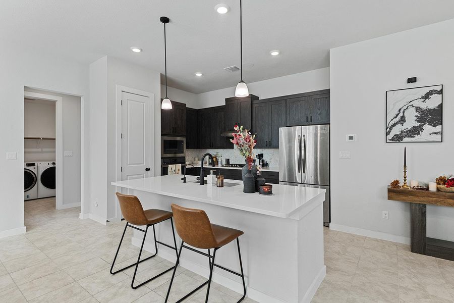 Kitchen featuring stainless steel appliances, a kitchen bar, tasteful backsplash, an island with sink, and hanging light fixtures
