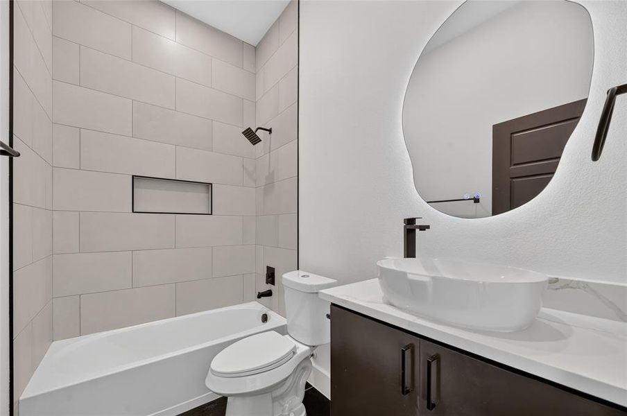 Bathroom featuring a vessel sink, dark wood-finish vanity with stone-look countertop, and an illuminated organic-shaped mirror Bathroom featuring a vessel sink, dark wood-finish vanity with stone-look countertop, and an illuminated organic-shaped mirror