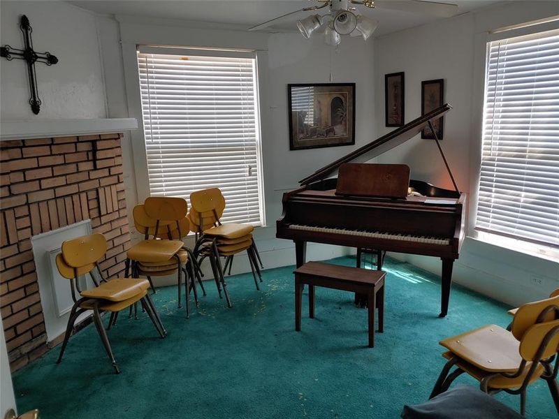 Room featuring brick fireplace with white mantel, two windows with blinds, and green carpeting Room featuring brick fireplace with white mantel, two windows with blinds, and green carpeting