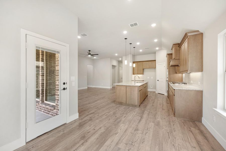 Open kitchen with center island, light wood cabinets, and hardwood floors open to living area with glass door