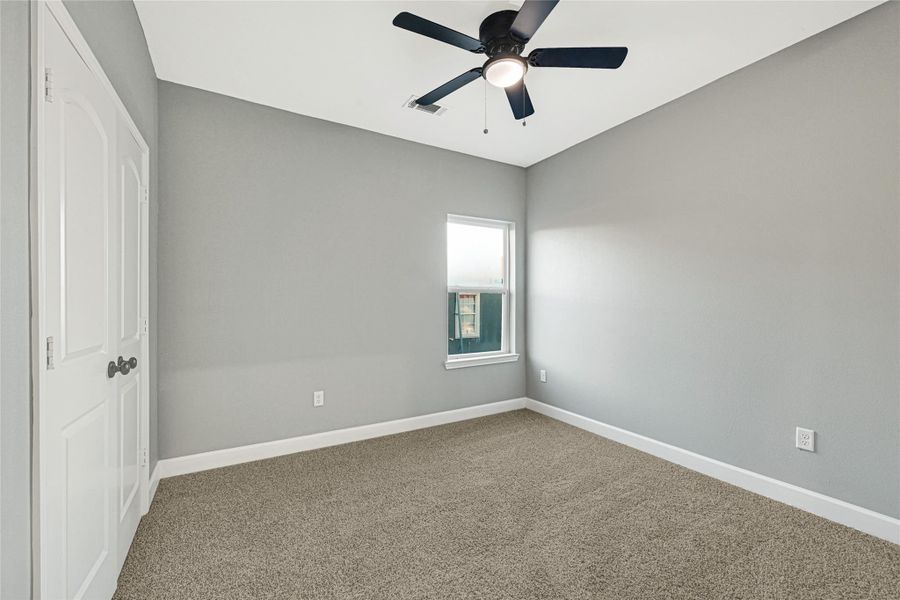 This room features a neutral color scheme with gray walls and carpet flooring. It has a ceiling fan and a single window for natural light, along with double doors for easy access.