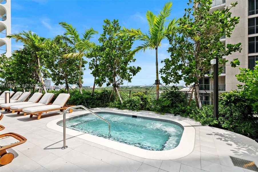 Relaxing outdoor jacuzzi surrounded by tropical landscaping and sun loungers for spa-like relaxation year-round.
