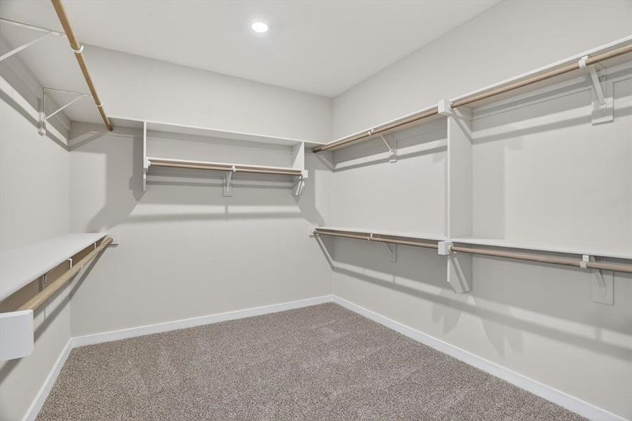 Spacious walk-in closet featuring white built-in shelving and multiple clothing rods Spacious walk-in closet featuring white built-in shelving and multiple clothing rods