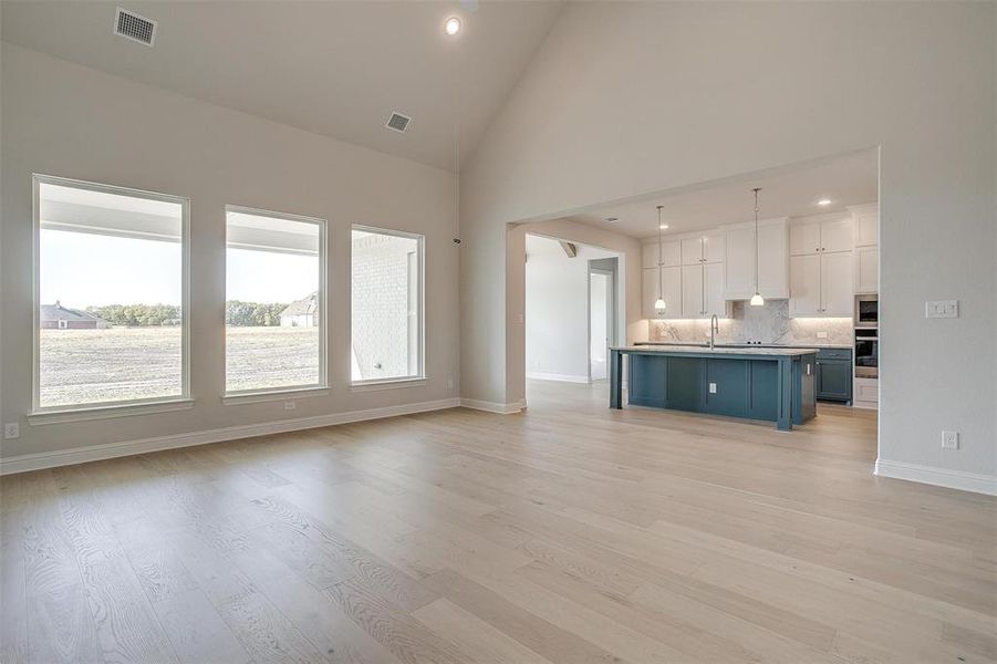 Unfurnished living room featuring sink, light hardwood / wood-style flooring, and high vaulted ceiling